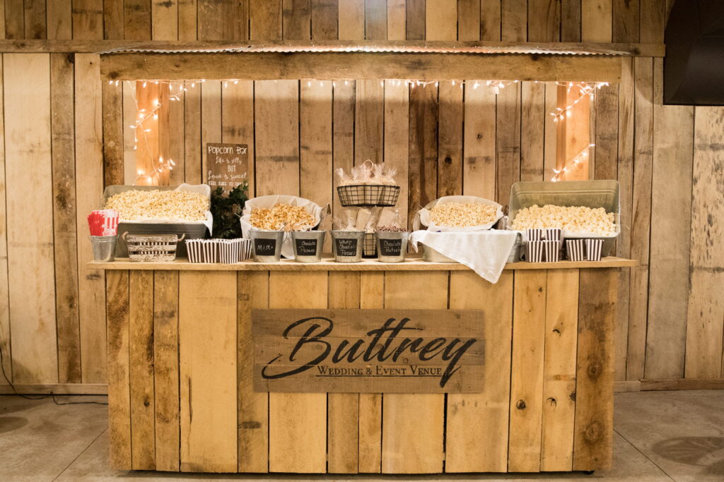 Popcorn bar at Buttrey Wedding & Event Venue, featuring various popcorn flavors in baskets and containers. Soft lighting creates a cozy atmosphere.