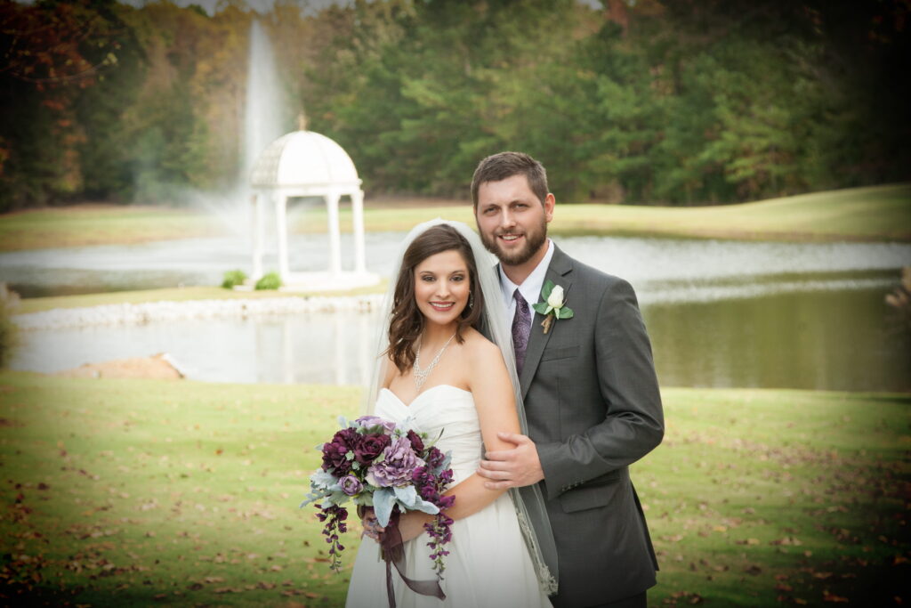 Couple embraces by a serene pond featuring a gazebo and fountain, captured during their wedding portrait session.