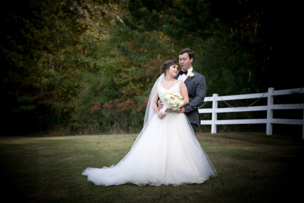 Bride and groom embrace in a serene outdoor setting, showcasing the bride's elegant white gown and bouquet against a lush backdrop.