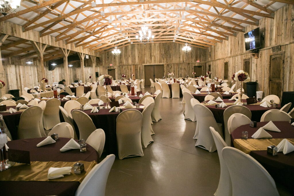 Elegant banquet hall featuring beautifully arranged tables with burgundy tablecloths and white chairs, set for a special event.
