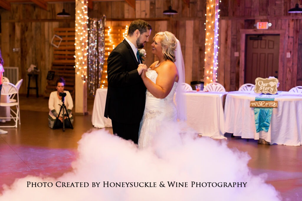 A bride and groom share their first dance amid swirling fog and twinkling lights at their wedding reception, creating a romantic atmosphere.