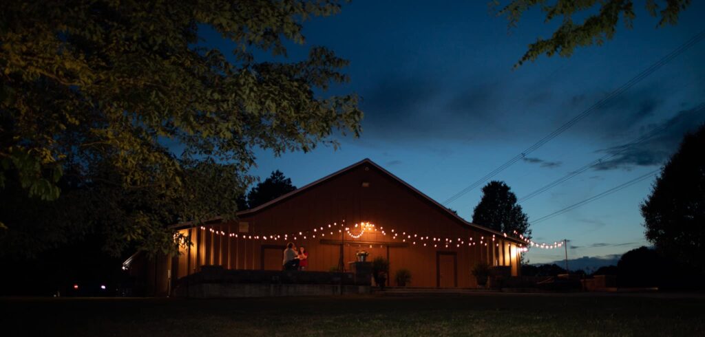 A warmly lit building decorated with string lights, set against a twilight sky, suggests a festive gathering or event.