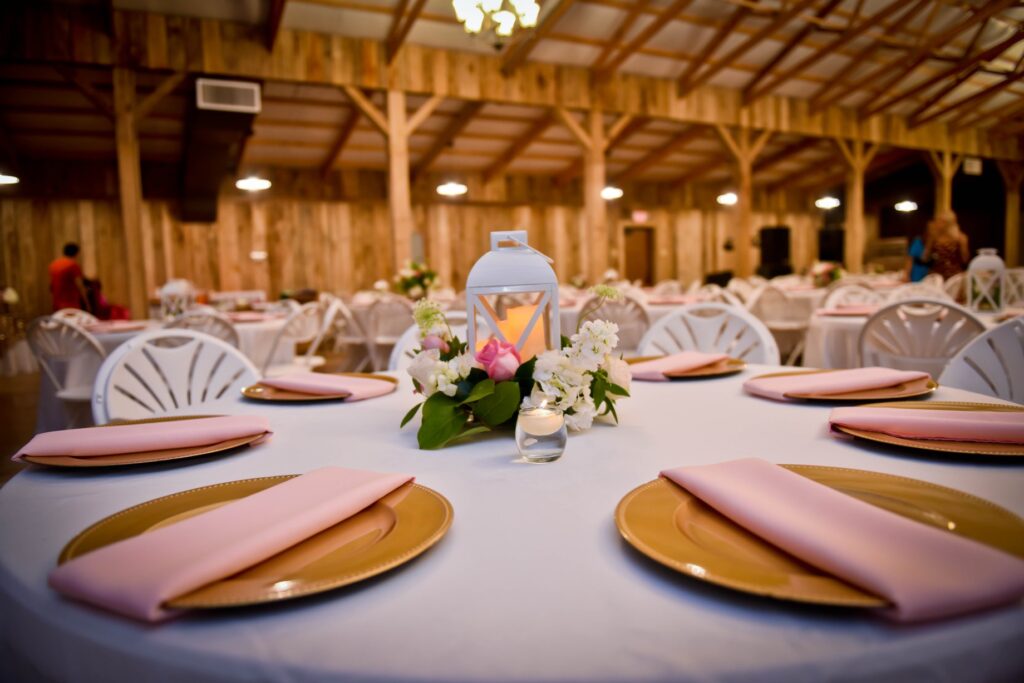 Elegant event setting with decorated tables, featuring floral centerpieces and soft lighting in a rustic venue. Suitable for gatherings or celebrations.
