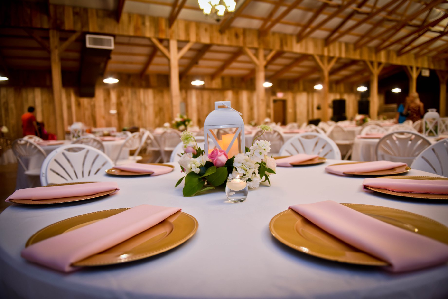 Elegant event setting with decorated tables, featuring floral centerpieces and soft lighting in a rustic venue. Suitable for gatherings or celebrations.