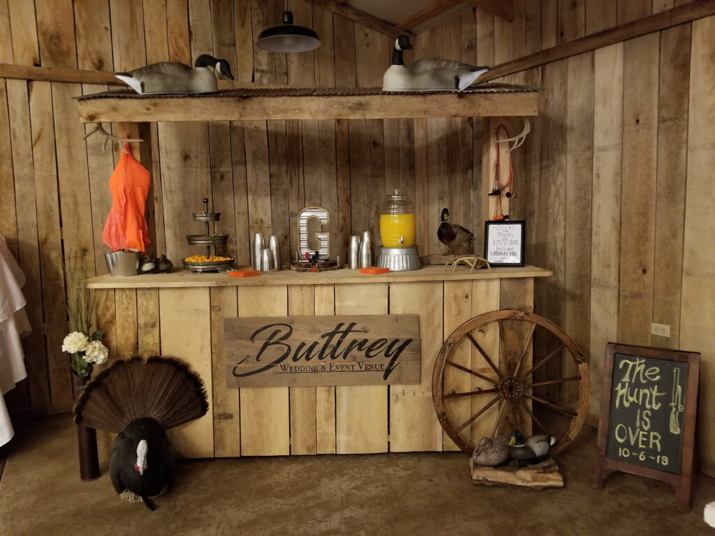 Rustic event space bar setup at Buttrey Wedding & Event Venue, featuring decorative ducks, a turkey, and a sign celebrating the conclusion of a hunting event.