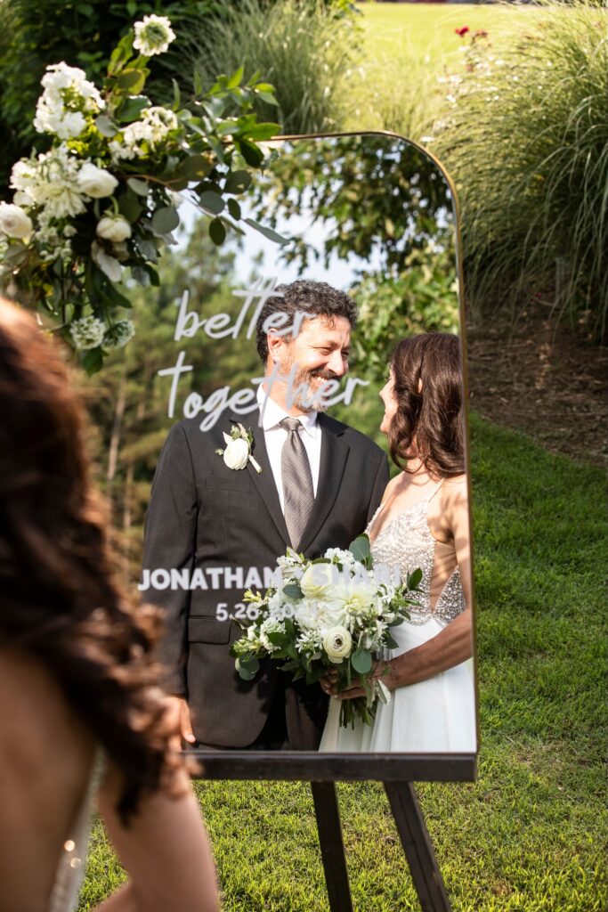 A couple shares a kiss under an ornate gazebo during their outdoor wedding ceremony, surrounded by their bridal party and guests in a lush garden.