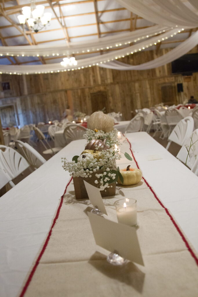 Festively decorated event space featuring a long table adorned with white flowers, candles, and decorative pumpkins, set for a gathering.