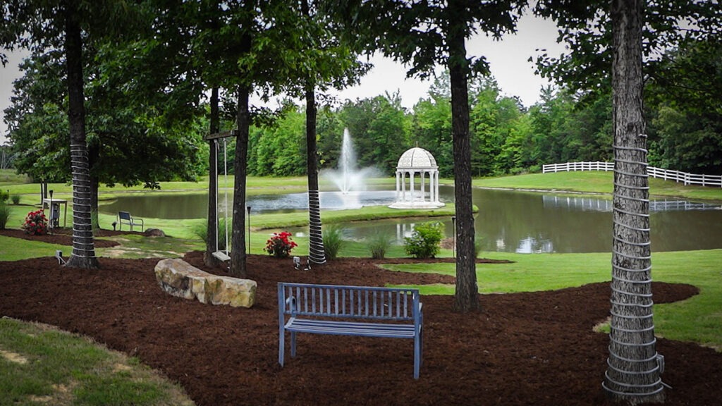 Scenic pond garden featuring a gazebo, fountain, and benches amidst trees and lush greenery, ideal for relaxation and gatherings.