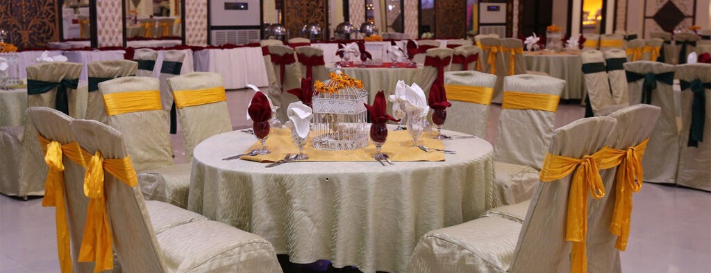 Elegant dining setup featuring round tables with gold and emerald decorations, poised for a formal event in a spacious venue.