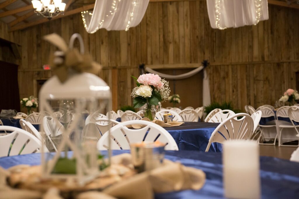 Elegant banquet hall setup featuring blue tablecloths, floral centerpieces, and white chairs, ideal for a wedding or special event.