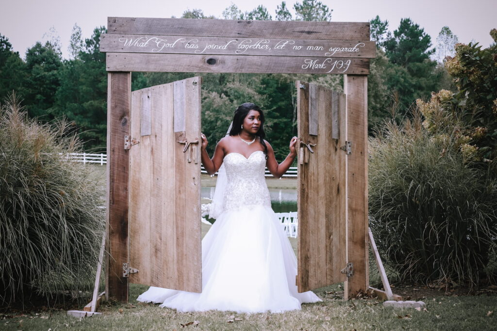 Bridal figure stands at an open wooden archway inscribed with "What God has joined together..." amidst a serene outdoor setting, symbolizing union.